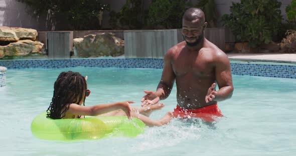 Happy african american father and daughter having fun in swimming pool with inflatable ring alt