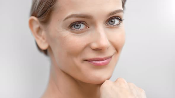Beautiful Female Face with First Wrinkles Smiling Looking at Camera Isolated at Light Background alt