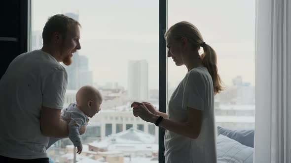 young couple playing with toddler standing by a large window