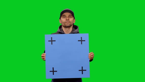 Casual Man in Baseball Cap Holding a Blank Blue Board with Tracking Points, Chroma Key
