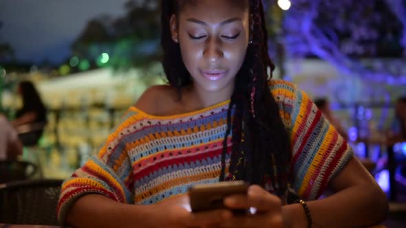 Black woman browsing smartphone in city at night alt