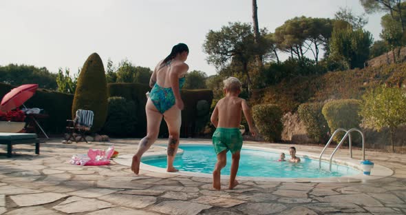Young woman running with children and jumping into the swimming pool alt