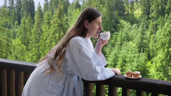 Beautiful Smiling Woman Relaxing at Hotel Wearing Bathrobe and Having Breakfast on Summer Terrace alt