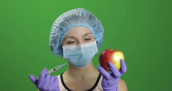 Female Scientist Makes a Injection with a Medicine Syringe in Apple alt