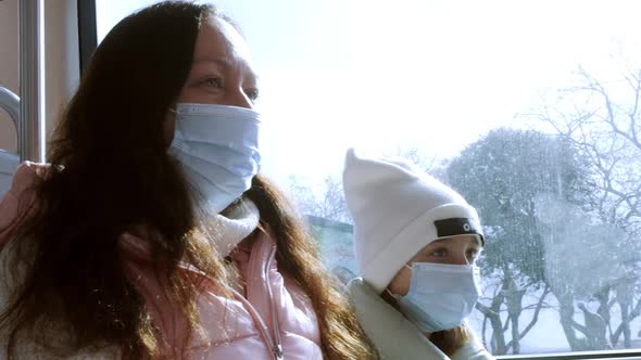 Mother and Daughter in Protective Masks Sitting Together in Public Transport alt