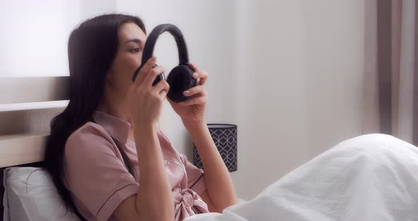 Woman Sitting in Bed Listening to Music Through Wireless Headphones and a Phone