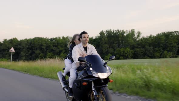 Beautiful Couple Rides Sport Motorcycle on the Road Near Field