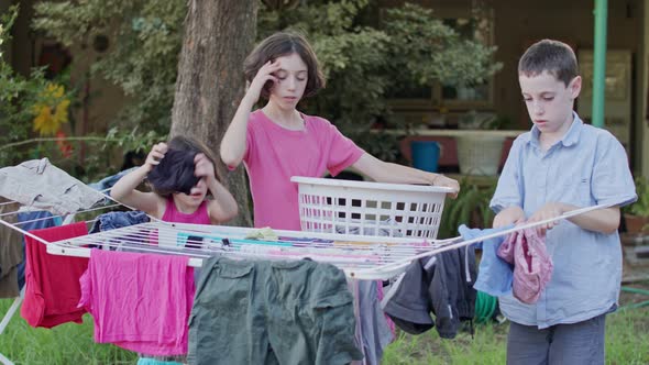 Three kids taking off laundry from the hanging line to the basket alt