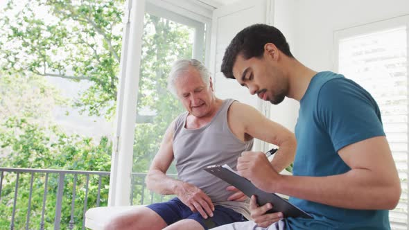 Caucasian senior man explaining while biracial male instructor making a note on clipboard alt