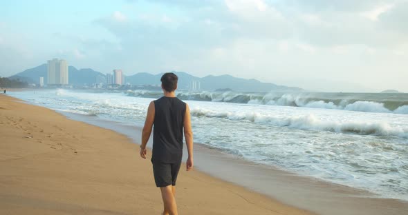 Man Walking Along the Sand Along the Coast in the Open Air Against the Backdrop of the Beautiful Sea alt