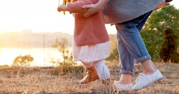 A Young Mother Walks By the Hand with Her Daughter in the Fresh Air. Happy Family Walking on Green alt
