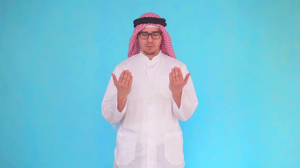 Arab Man Stands on a Blue Background and Turns To God Reading a Prayer alt