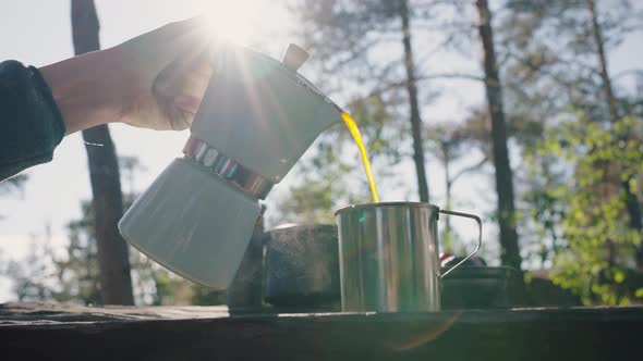 Person Hands Pour Hot Drink to Mug on Table Against Forest alt