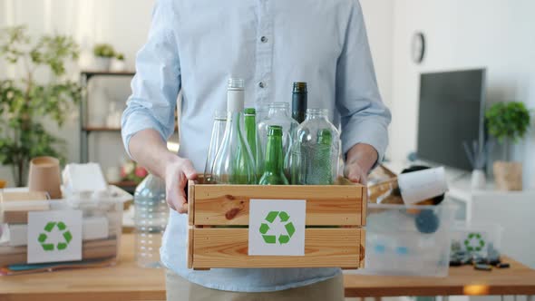 Closeup of Male Hands Holding Wooden Box with Glass Bottles for Recycling Standing at Home alt