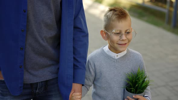 Father Holding Son Hand and Child is Holding the Plant in a Pot Telling Father Stories From School alt