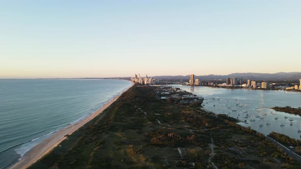 Coastal nature parklands dividing a boat harbor and coastline with an urban city skyline rising abov alt