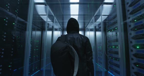 Hacker with a Backpack Walking Through Rows of Rack Servers alt