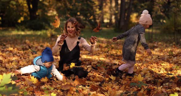 Gorgeous Young Mother with Two Kids Enjoying Sunny Autumn Day on the Foliage