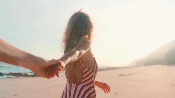 Young Caucasian Woman Smiling Stretches Out Hand to Man and Leads Him Along alt