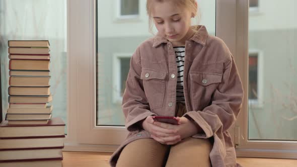 Girl Sitting on the Windowsill and Looking at the Phone