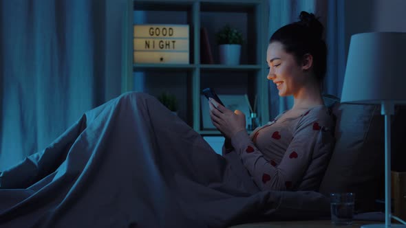 Teenage Girl in Pajamas with Phone in Bed at Night alt