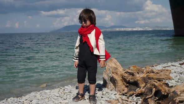 Stylish Child a Boy in a Black Jumpsuit and a Red Scarf Stands on the Beach