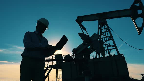Male Worker Is Making Calculations at the Oil Pumping Site. Fossil Fuel, Crude Oil Concept alt