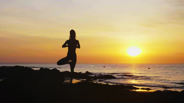 Young Woman in Tree Pose with Hands in Namaste on Ocean Beach at Sunset