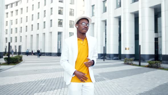 Joyful black man in glasses and white wireless headphones listens to music alt