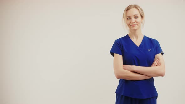Positive Blonde Healthcare Worker Woman in Dark Blue Uniform Looking at Camera and Crossing Her Arms alt