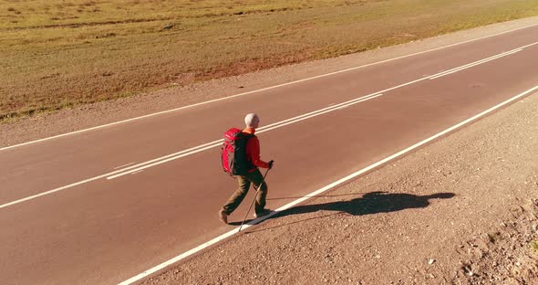 Flight Over Hitchhiker Tourist Walking on Asphalt Road. Huge Rural Valley at Summer Day. Backpack alt