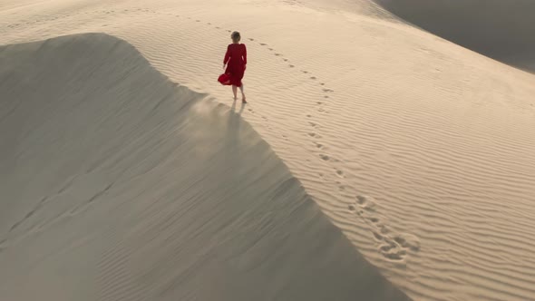  Aerial View of the Woman Walking By the Peak of Sand Dune at Sunset alt