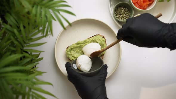 Cook in Gloves Puts Poached Eggs on Toast with Guacamole alt