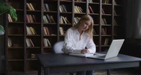 Business Woman in a White Shirt Works at a Laptop and Takes Notes alt
