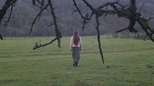 Young woman in skirt going in field. Branches, mountain forest. Alone on nature, freedom 4K slow