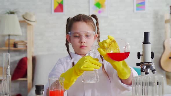 Girl Teen Blogger in a White Coat and Glasses in the Laboratory Mixes the Reagents alt