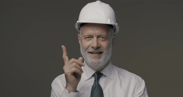 Cheerful businessman and engineer wearing a safety helmet and pointing upwards