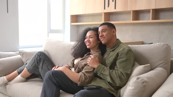 Side View of the Multiracial Couple Chilling on the Couch Watching Movie in the Studio Apartment alt