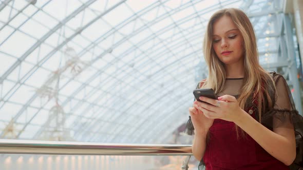 Happy Teenage Girl Holding Bags with Purchases, Smiling While Looking at Phone in Shopping Center alt