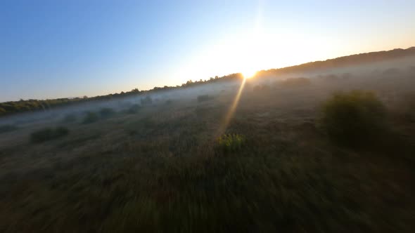 Fast Low flying above sloping field at beautiful summer sunrise