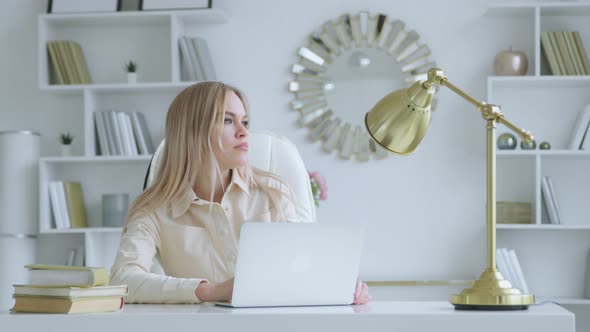 Thinking girl with laptop at the desk at home office. Young woman with laptop at home alt