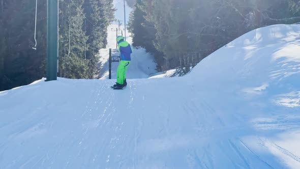 Boy on Snowboard Go Up Holding Tbar Ski Lift at Skiing Resort alt