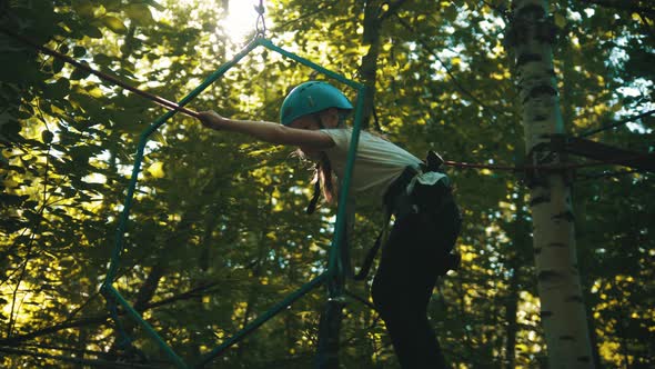 A Little Girl Walking on the Rope Bridge and Holding By the Ropes alt