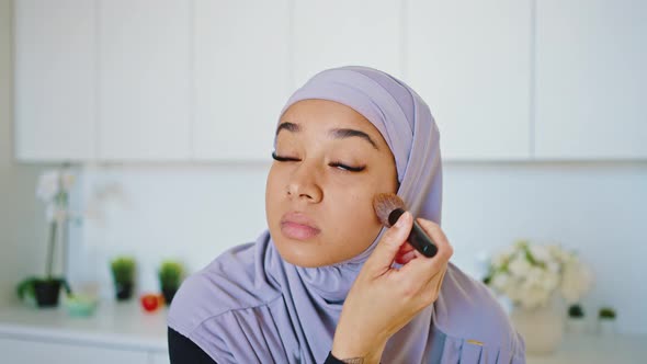Close Portrait of a Beautiful and Young Muslim Woman Applying Powder with a Brush to Her Face While alt