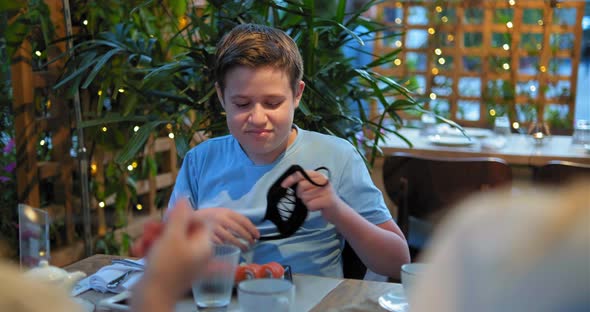 boy in t-shirt takes off designed face mask and eats sushi alt