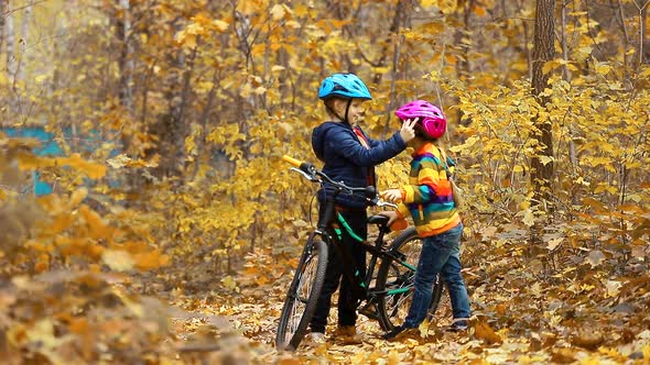 The older sister helps the younger girl put on a safe helmet before Cycling on an autumn day