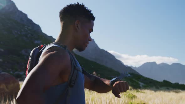 African american man cross country running in mountain countryside using smartwatch alt
