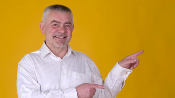 Cheerful elderly gray-haired man point fingers hands aside on copy space workspace area alt