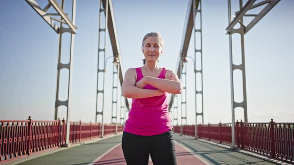 Senior Woman Crosses Arms Standing on Pedestrian Bridge alt