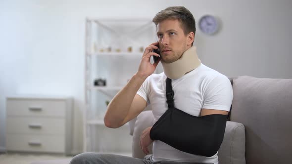 Man in Arm Sling and Foam Cervical Collar Talking on Cellphone, Upset With News alt